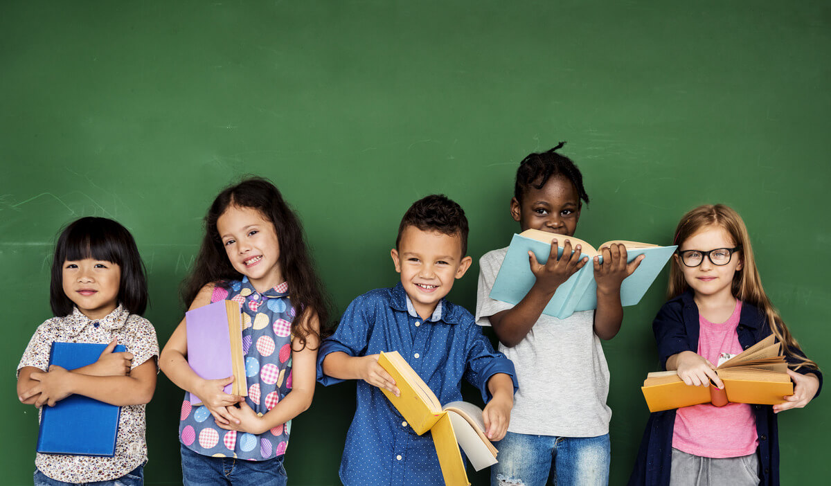 Five kids standing in front of a chalkboard with books in their hands.