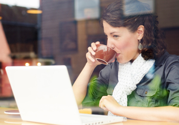 Woman drinking from a coffee cup, while working on her laptop.