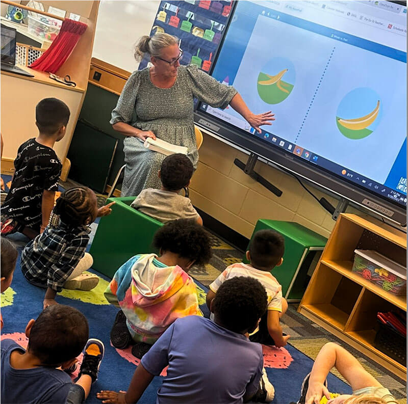 Teacher using smartboard to teach students, sitting in front of her.