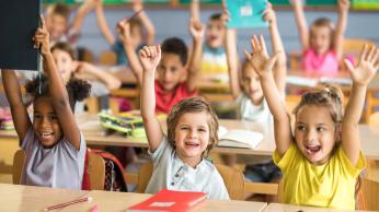 Kids smiling in class, raising their hands.