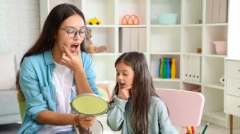 Woman and child practicing oral language into a mirror.