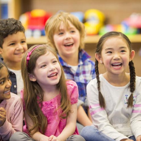 Children sitting on classroom floor, laughing.