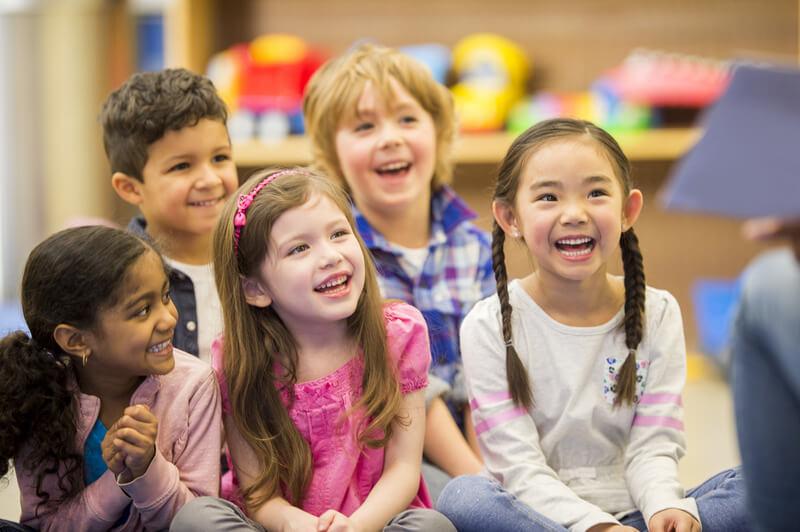 Children sitting on classroom floor, laughing.