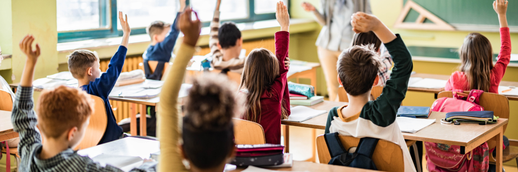 Students raising their hands in classroom.