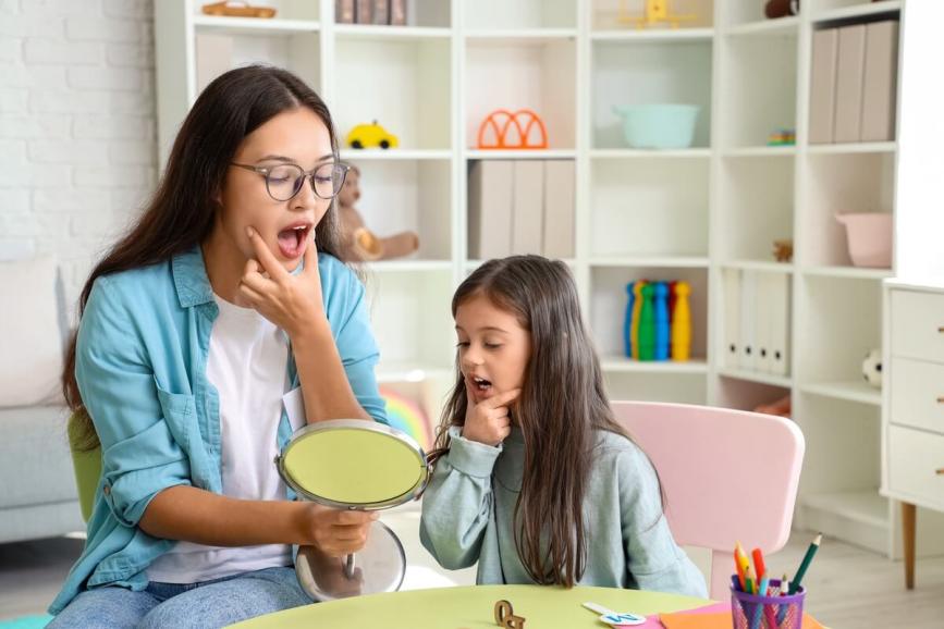 Woman and child practicing oral language into a mirror.