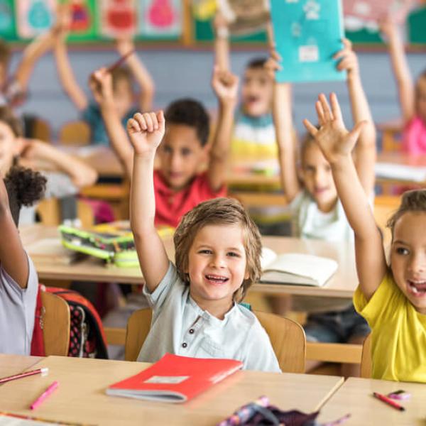 Kids smiling in class, raising their hands.